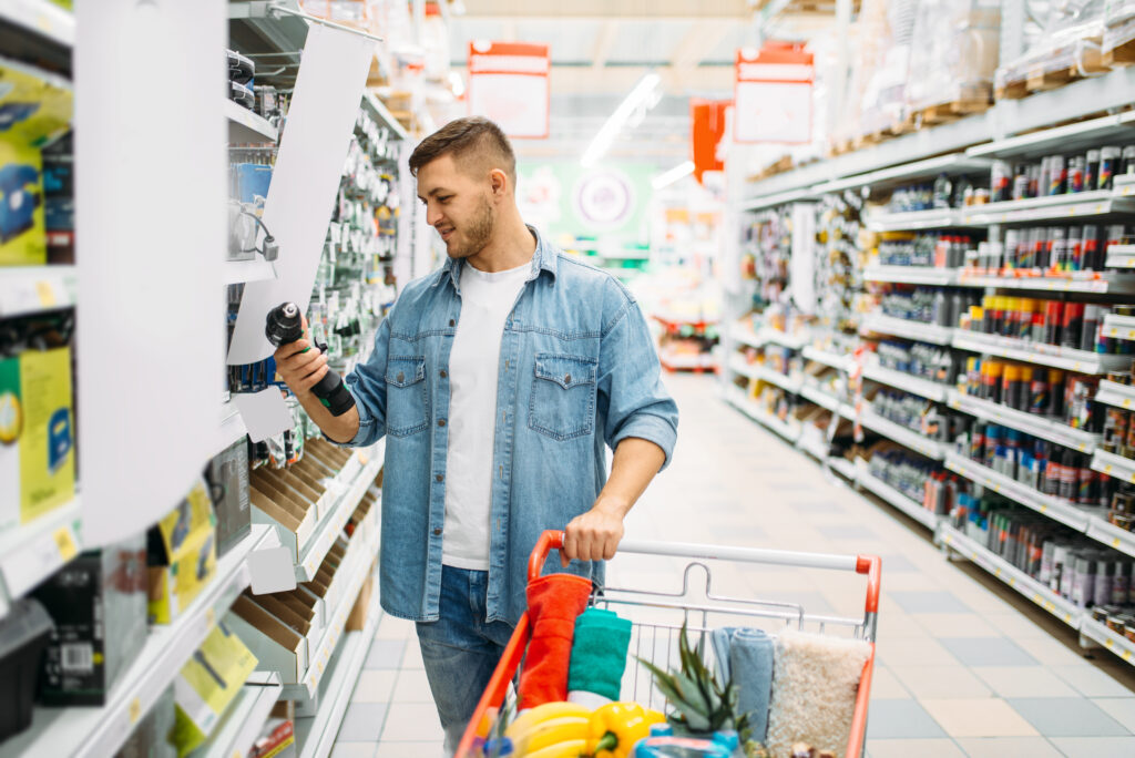 Man choosing electric screwdrivers, power tools department in supermarket, family shopping. Customer with cart in shop